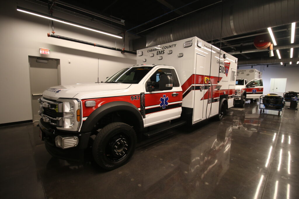 Interior of a modern EMS facility with white and red ambulances parked side by side in a glossy garage.